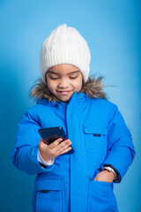 young Latina looking at smart phone and wearing blue winter clothes. concept of addiction to smart phones