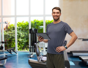 Fototapeta na wymiar fitness, sport and healthy lifestyle concept - smiling man in sports clothes holding tablet pc computer over gym background