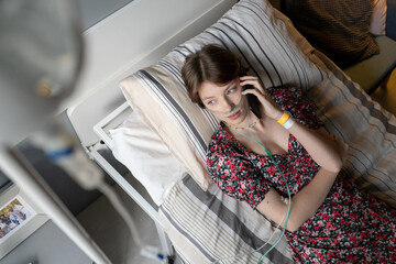 High angle view of sick girl having a conversation on mobile phone while lying on bed at hospital...
