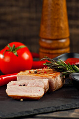 Steak with sliced tomatoes on a cutting board. Meat on a dark wooden background. Food, sauce, salt, pepper and spices on an old shabby table.