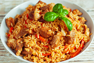 Pilaf in a white plate on a light background. Rice with basil on an old wooden board. Food on shabby wooden table.