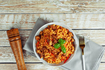 Pilaf in a white plate on a light background. Rice with basil on an old wooden board. Food on shabby wooden table. Copy space and war place for text near food.