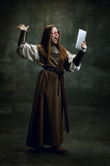 Vintage portrait of young beautiful girl in image of medieval warlike woman using modern gadget...