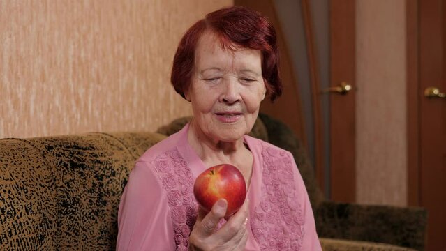 Portrait of an octogenarian woman at home with a red apple in her hands on the sofa.
