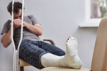 A sad man with a broken leg sits on a chair. Illness concept.