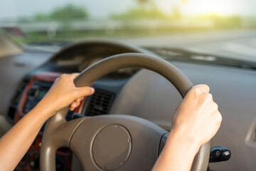Naklejka premium Hand female on the steering wheel of a car while driving the windshield and road. Close up of woman hand presses the horn on the steering wheel on her car.