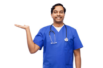 healthcare, profession and medicine concept - happy smiling indian doctor or male nurse in blue uniform holding something imaginary on empty hand over white background