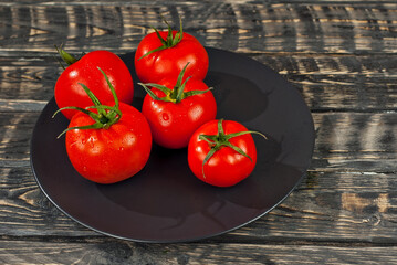 Red tomatoes on a black wooden background. Vegetables on an old shabby table. Tomatoes in a black dish.