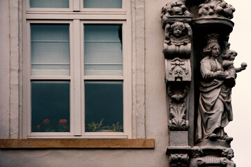 Detail of an old window with red roses behind the glass, ornamented with baroque sculpture in the city of Bruges, Belgium.