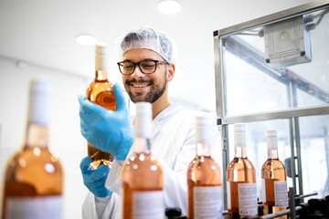 Factory worker or technologist checking quality of bottled wine in alcohol beverage bottling...