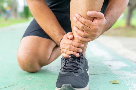 Young male in sports outfits black injured his ankle during exercise in the park. Low section of sports man suffering from flipped ankle while sitting on track during. Accident from exercise concept.