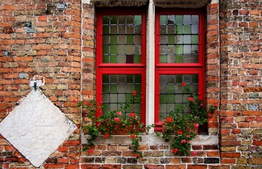 Old wooden window painted red with checkered glass. Flower pot and orange brick facade. Bruges, Belgium