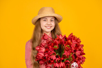 cheerful child in hat hold spring tulip flowers on yellow background