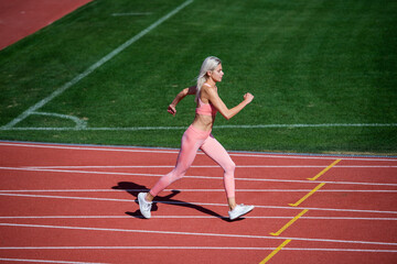 Fototapeta premium Great progress. woman sport trainer in motion. speed and energy. stamina. sexy runner in fitness sportswear. sprinting on outdoor arena racetrack. training and workout. athletic female coach running