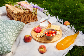 leisure and drinks concept - close up of food, drinks and basket on picnic blanket on grass