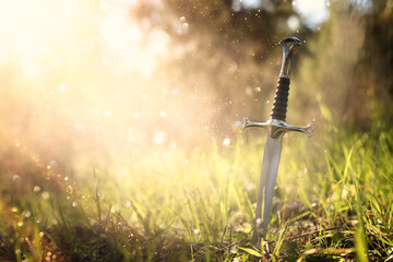 mysterious and magical photo of silver sword in the England woods and light flare. Medieval period...