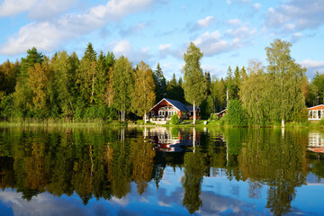 Fototapeta na wymiar Wunderschöner Blick auf Stukas Ferienhäuser vom See aus in Schweden mit Spiegelungen im Wasser vom Boot aus Im Schwedenurlaub