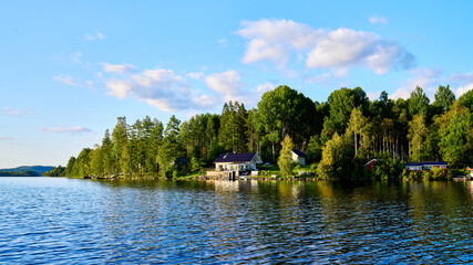 Fototapeta na wymiar Wunderschöner Blick auf Stukas Ferienhäuser vom See aus in Schweden mit Spiegelungen im Wasser vom Boot aus Im Schwedenurlaub