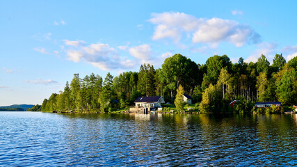 Fototapeta premium Wunderschöner Blick auf Stukas Ferienhäuser vom See aus in Schweden mit Spiegelungen im Wasser vom Boot aus Im Schwedenurlaub