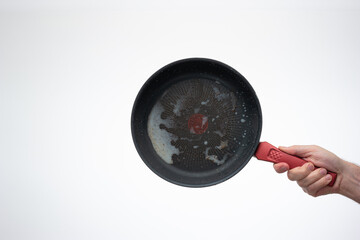 Dirty oily burnt metal frying pan held in hand by male hand - obrazy, fototapety, plakaty