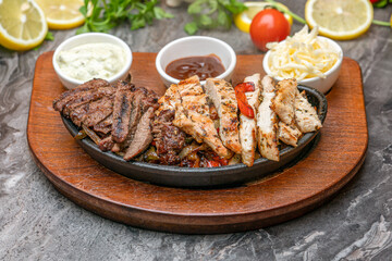 Meat and chicken fajitas on black stone plate with sauces