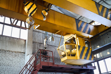 Yellow with black stripes overhead crane with linear traverse and hooks at petrochemical enterprises chemical plant workshop. Crane operator cabin and hooks and jib crab trolley. Landing staircase. - obrazy, fototapety, plakaty