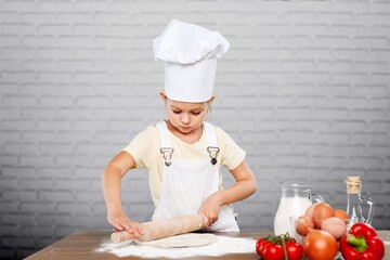 Toddler child playing with the dough in the kitchen dressed as a chef. Child baking a cake
