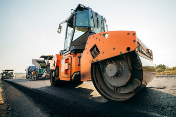 Vibratory asphalt roller compactor compacting new asphalt pavement. Road service repairs the highway