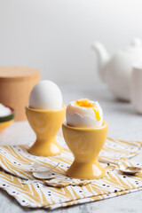 Soft-boiled eggs in yellow egg cups for breakfast, natural and healthy eating, cholesterol, protein, liquid yolk, natural light with copy space
