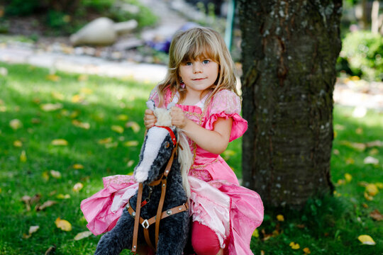 Little preschool girl hugging with rocking horse toy. Happy child in princess dress on sunny summer day in garden. Girl in love with her favourite old vintage toy animal.