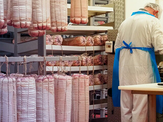 worker manufacturing, stuffing and tying bacon and other delicatessen in cured meats production...