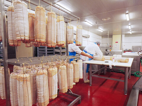 worker manufacturing, stuffing and tying bacon and other delicatessen in cured meats production facility
