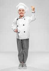 cooking, culinary and profession concept - happy smiling little girl in chef's toque and jacket over grey background