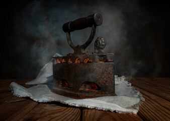 An old vintage iron iron with coals inside and steam on a wooden table with a linen napkin.