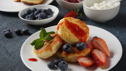 Cottage cheese fritters or syrniki or pancakes with fresh blueberries, strawberries and strawberry jam. Tasty dessert or sweet breakfast. Russian, Ukrainian cuisine