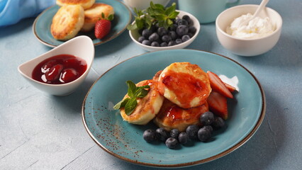 Cottage cheese fritters or syrniki or pancakes with fresh blueberries, strawberries and strawberry jam. Tasty dessert or sweet breakfast. Russian, Ukrainian cuisine