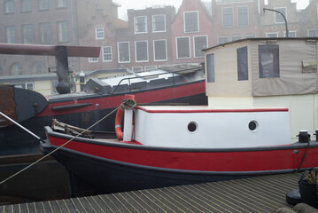 Fototapeta na wymiar 12 January 2022, Leiden, the Netherlands, A misty day, with an old boat on the front and mist covering the canal and the buildings in the background