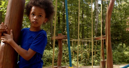 Obraz premium The boy deftly moves along the hinged rope path on the playground, tenaciously grabbing the ropes with his hands. Harmonious development of children's body through outdoor activities.