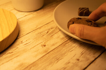 お皿に載ったチョコチップクッキーとチョコレート、人の手