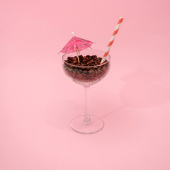 Cocktail glass filled with coffee beans with straw and paper umbrella. Party concept.