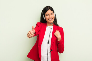 young pretty hispanic woman feeling proud,smiling positively with thumbs up. telemarteker concpet