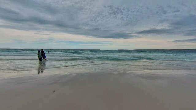 White Sands Hyams Beach, Jervis Bay in Australia under dark clouds with sea waves, people swimming and walking on the beach