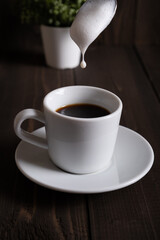 Milk foam drips from a spoon into a cup of espresso macchiato.