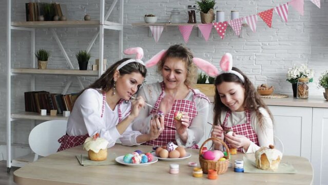an adult mother and her daughters paint Easter eggs together at home in the kitchen and prepare for the Easter holiday. Rabbit ears on the head