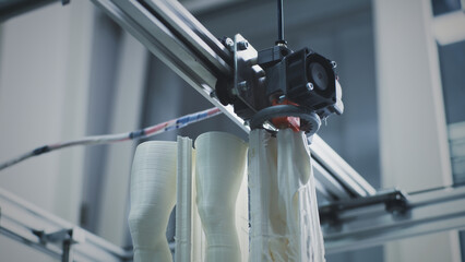 From below modern 3D printer printing legs of plastic statuette in workshop of modern creative design studio