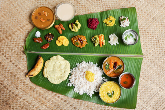Traditional Onam sadhya rice Sambar, Rasam, parippu dal curry ghee Pappadom Payasam on banana leaf Onam Vishu Pongal Diwali festival vegetarian food Kerala Tamil Nadu South India.