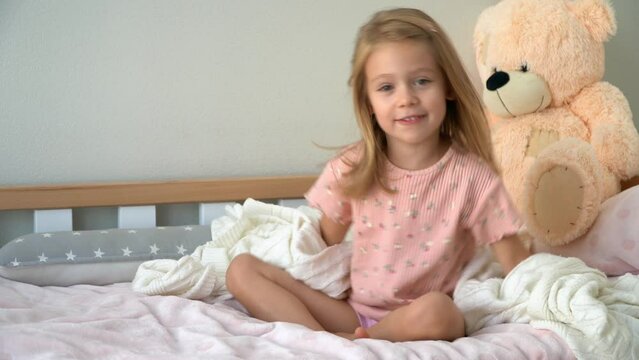 Little girl hids under blanket in bed fools and laughs. Happy child plays after sleep