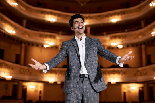 talented young man performing opera or singing at a concert or show, feeling romantic, artistic and passionate. caucasian bearded brunette guy in stylish elegant gray suit gesturing with hands