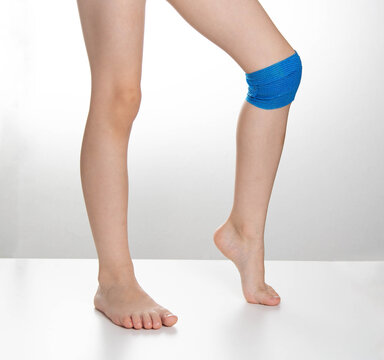 Blue elastic bandage on the knee joint on the child's leg. White background, treatment of knee pain and sprain, close-up