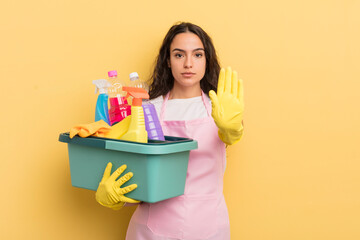young pretty hispanic woman looking serious showing open palm making stop gesture. housework an...